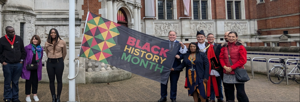 Mayor Perry and residents stand next to the Black History Month flag outside the Town Hall.