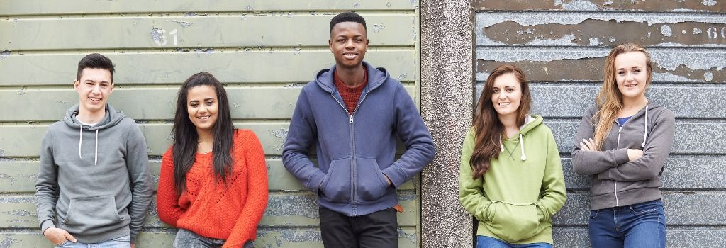 Young people stand in a row in front of a wall.