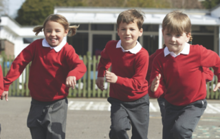 A row of primary school children running in a playground wearing their school uniforms.