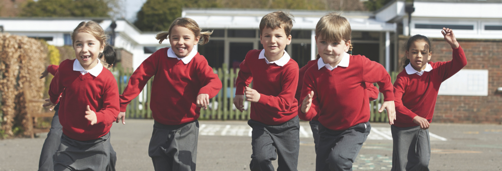 A row of primary school children running in a playground wearing their school uniforms.