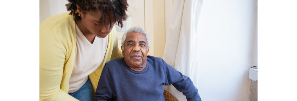 Man sitting down and being helped by a carer.